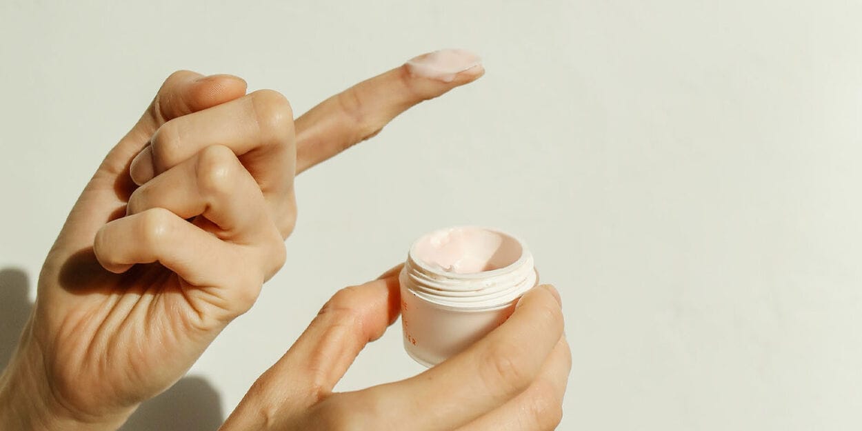 Rechterhand houdt klein (open) potje crème vast en linker wijsvinger heeft wat crème op de vinger