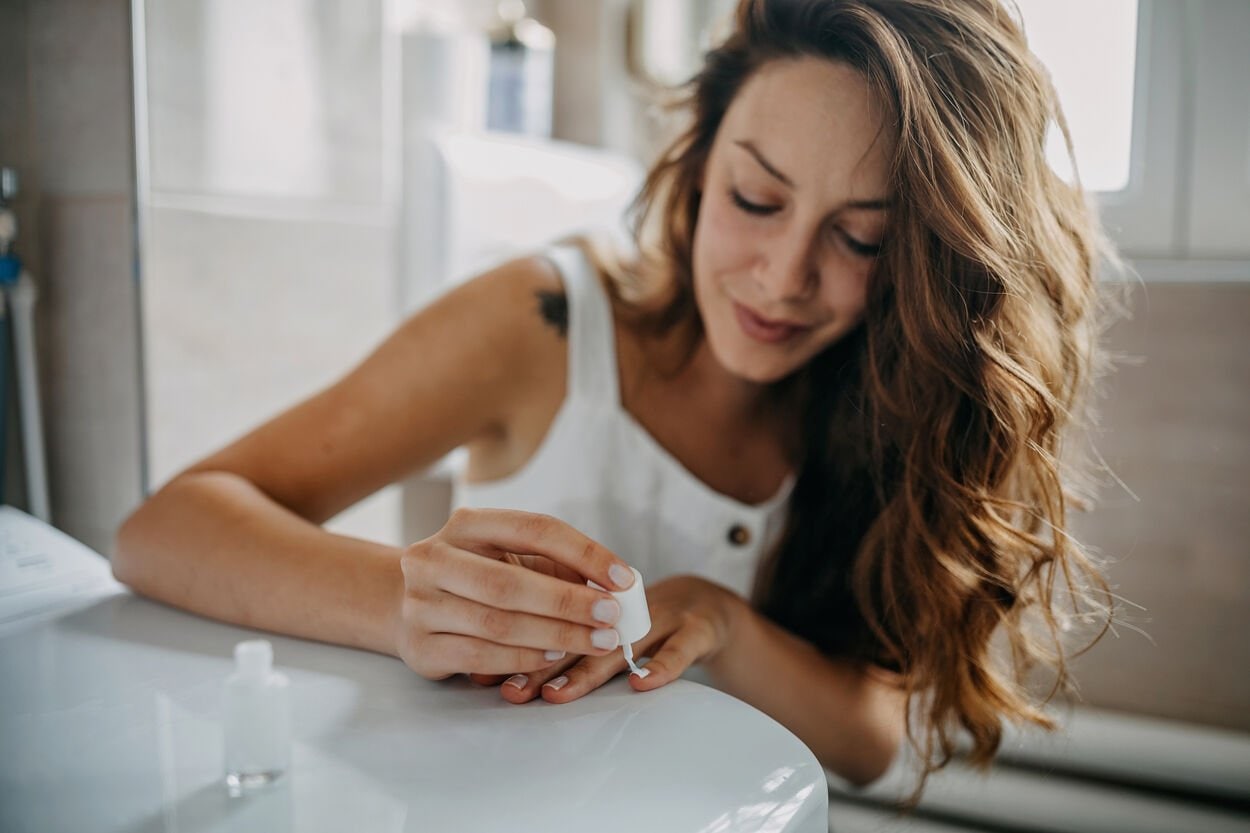 Vrouw die haar nagels lakt, waarbij er nagellak op haar kleding komt, wat ze graag wil verwijderen.