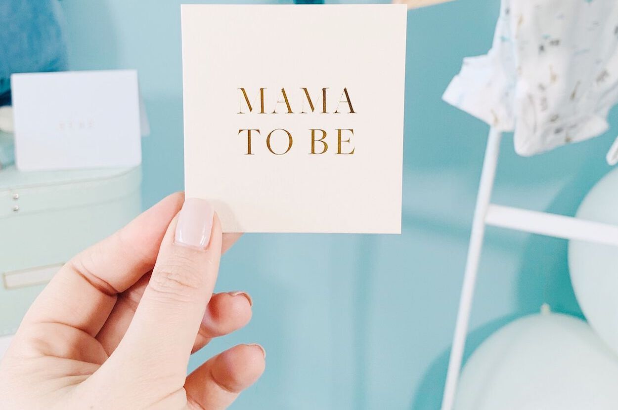 Vrouw die een papiertje vasthoudt waarop staat: 'mama to be'.