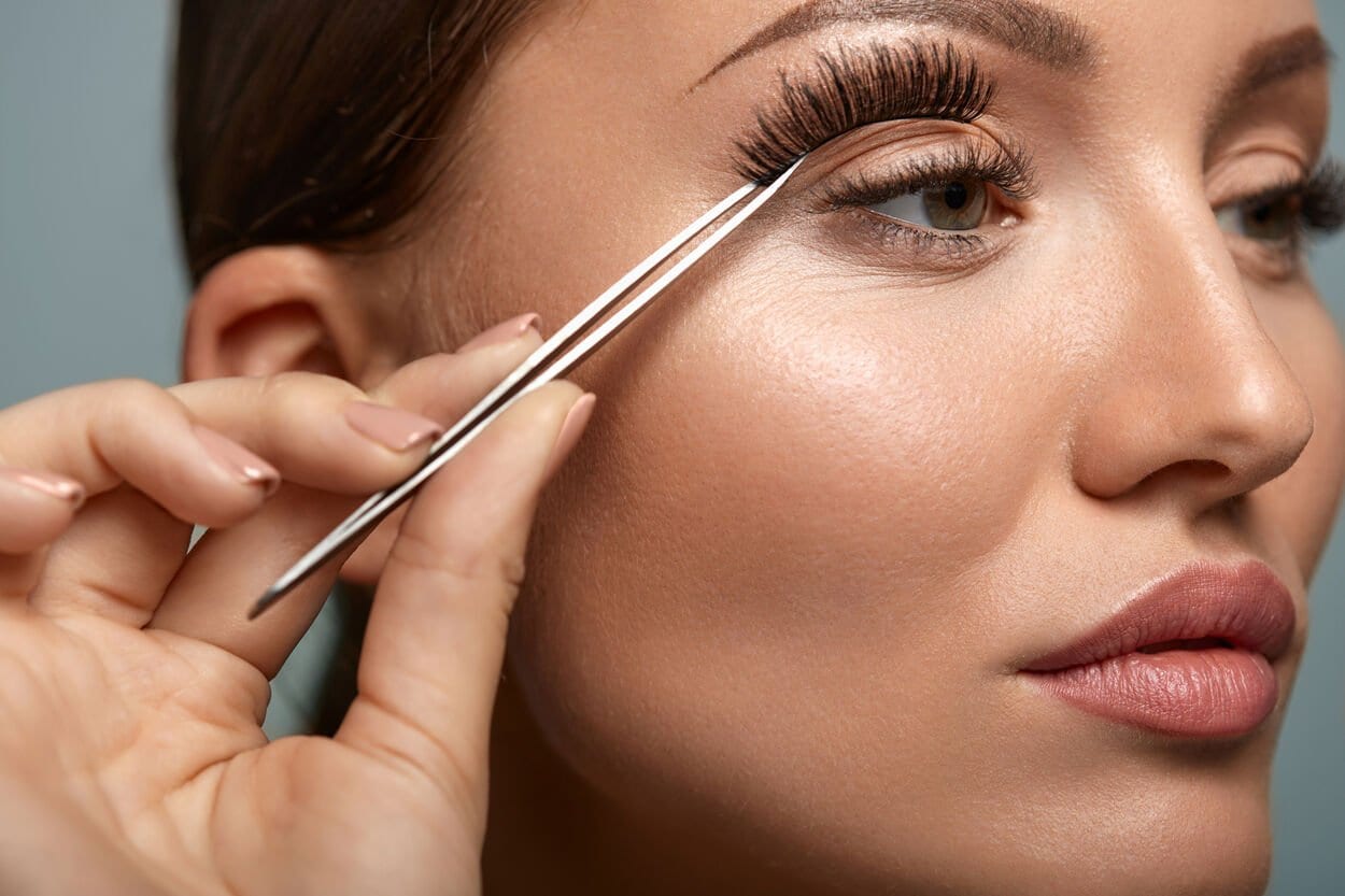 Vrouw die met een wimpertang haar nepwimpers gaat plakken.