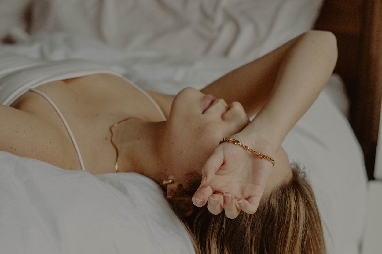 Vrouw aan de rand van haar bed met haar arm over haar gezicht. Ze voelt zich licht in haar hoofd door een lage bloeddruk.