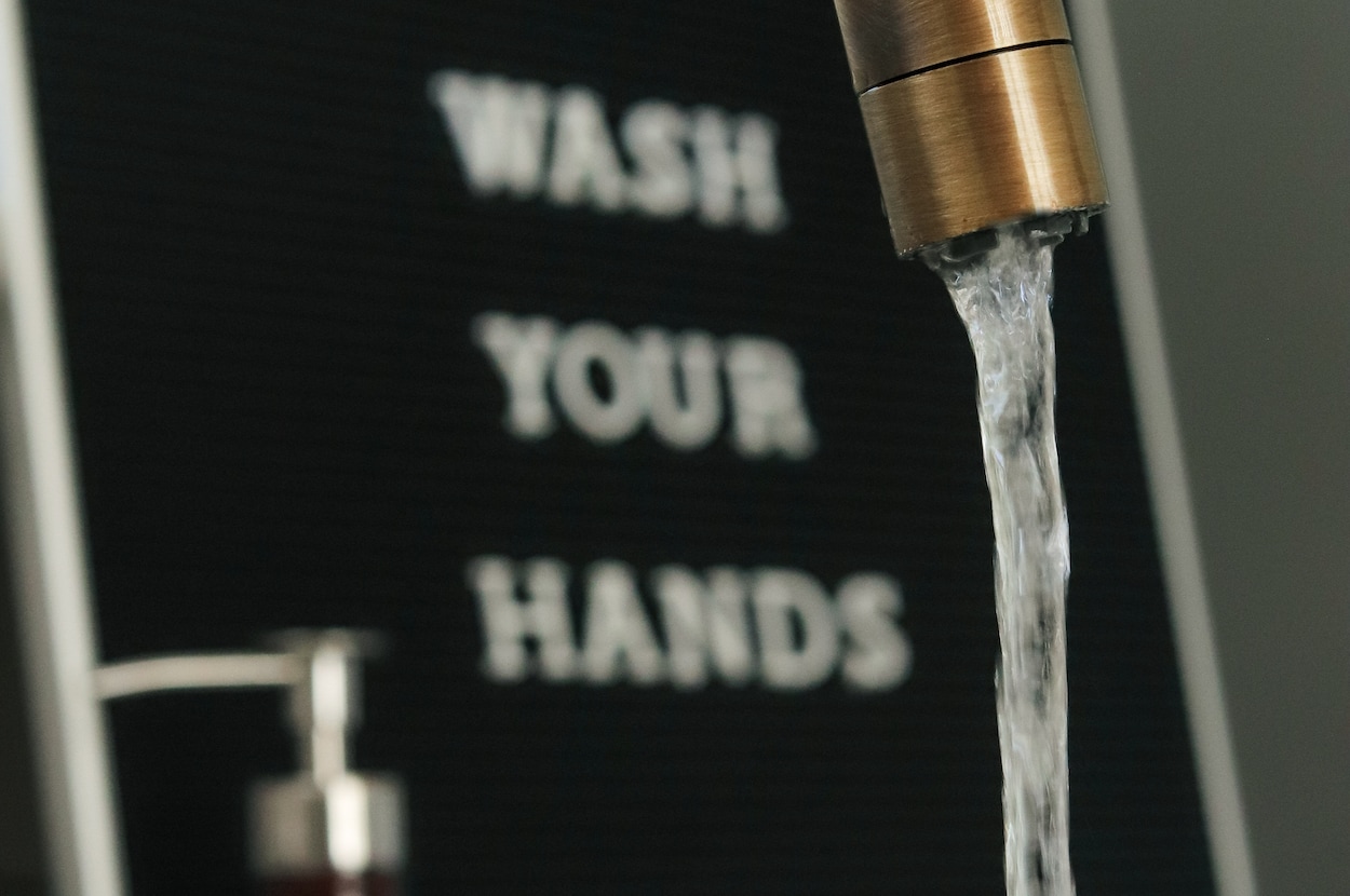 lopende kraan met in de achtergrond een bord met &#39;wash your hands&#39;