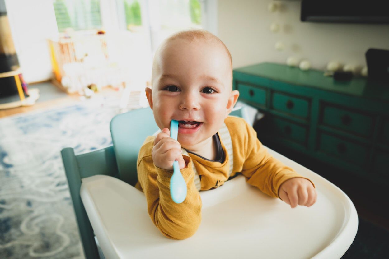 Baby in een kinderstoel met een tandenborstel. Zijn eerste melktanden komen door.