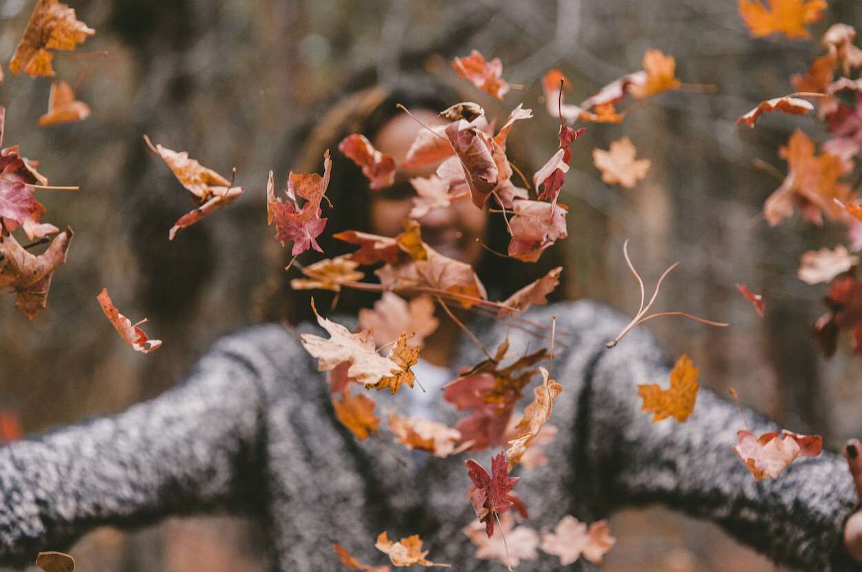 vrouw gooit herfstbladeren voor zich omhoog