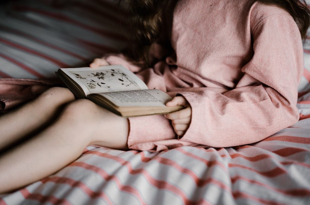 Meisje zit op bed en leest een boek