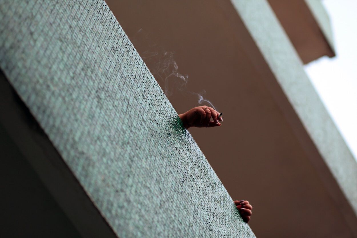 hand met brandende sigaret over de rand van een balkon