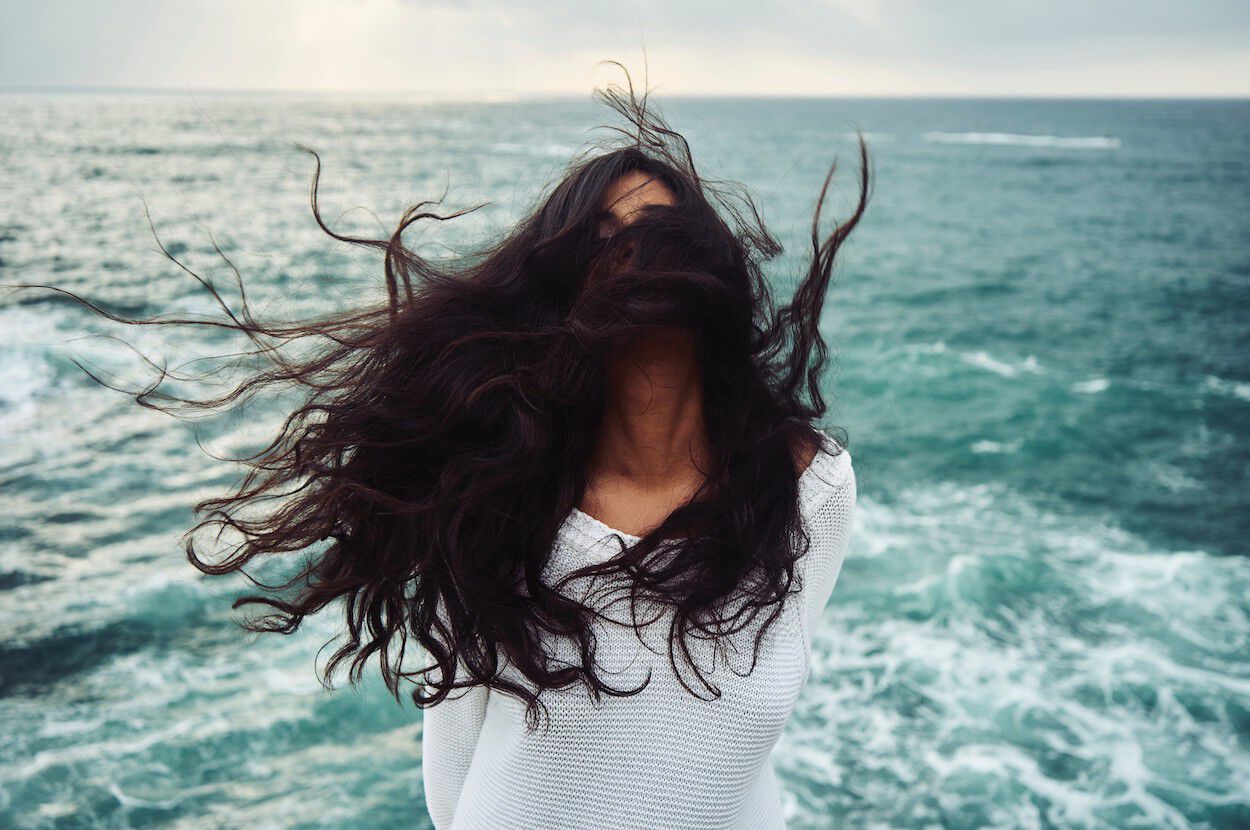 vrouw met witte trui in wind voor de zee