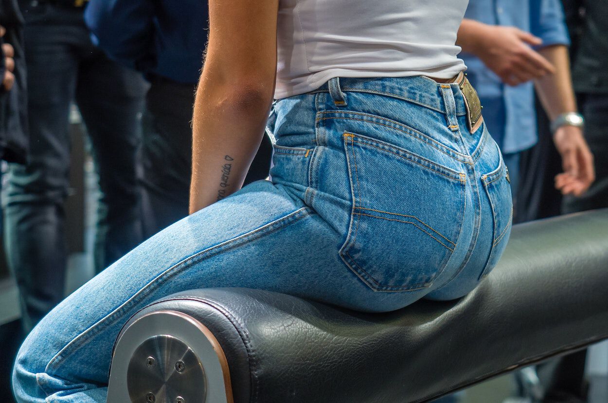 Vrouw in een denim jeans die op een rond bankje zit.
