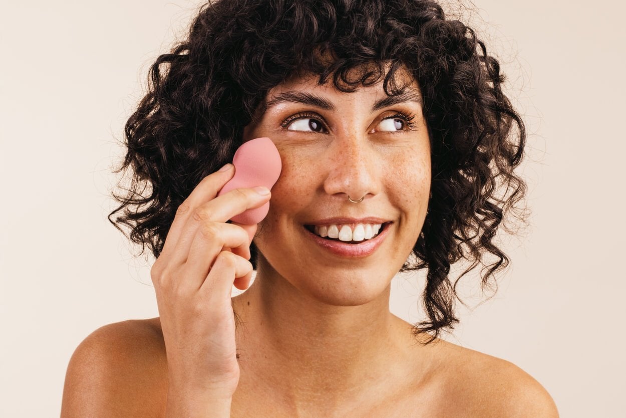Vrouw die met een beauty blender BB cream aanbrengt als onderdeel van haar make-uproutine.