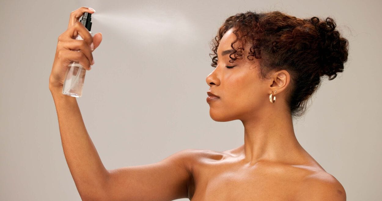 Vrouw die fixing spray over haar make-up aanbrengt.