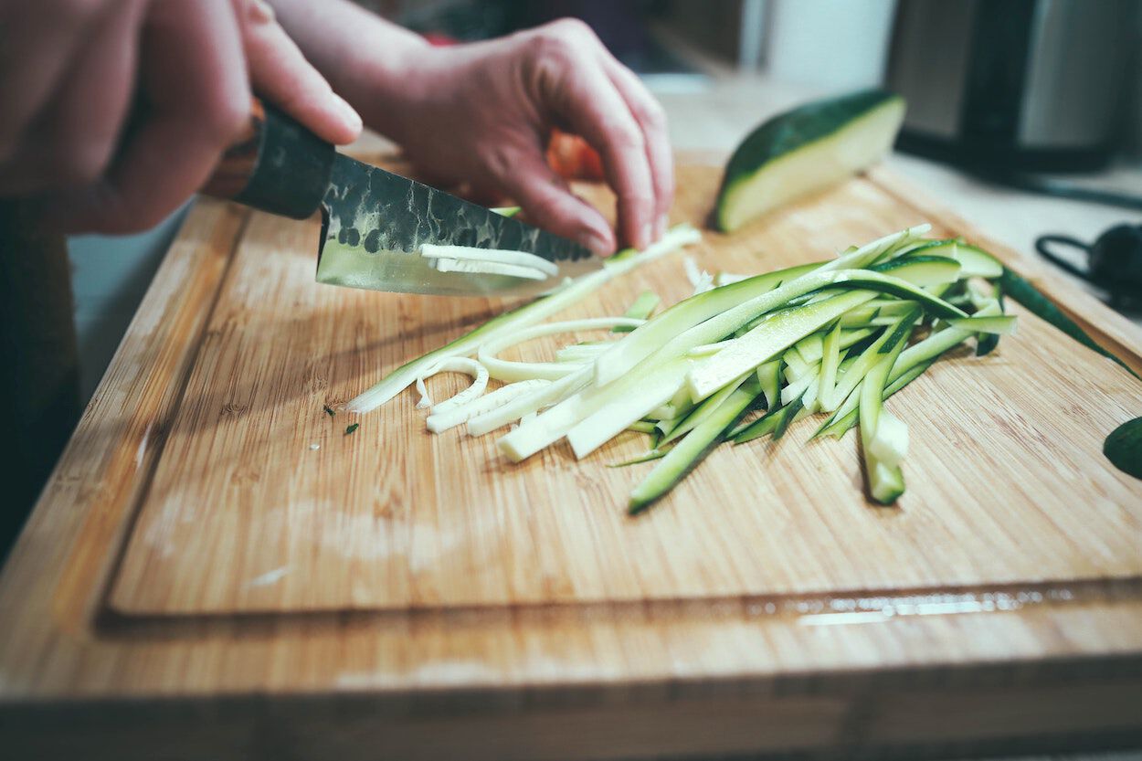 Vrouw is een courgette aan het snijden op een houten snijplank. Ze volgt een keto dieet.