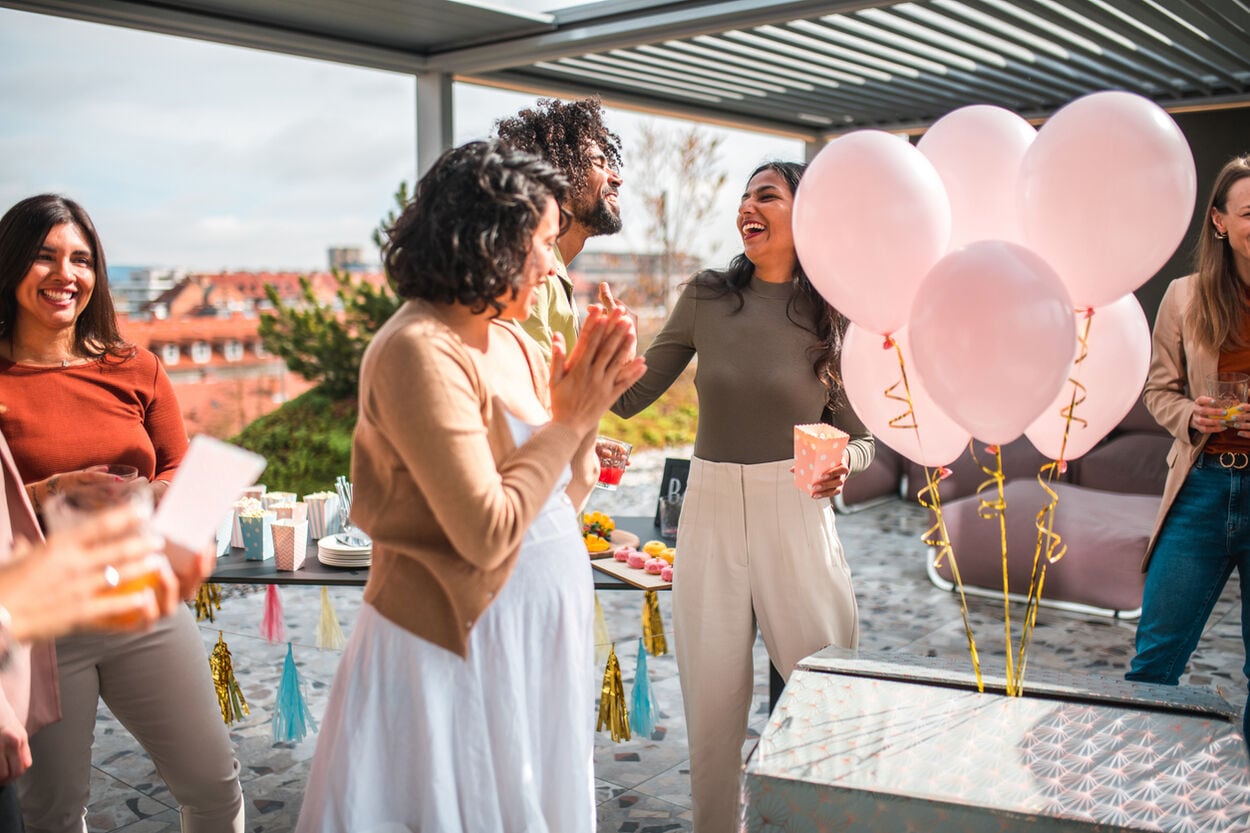 Zwangere vrouw bij haar gender reveal die voor een geopende doos vol roze ballonnen staat.