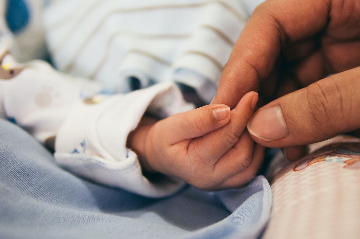 Een baby die net bevallen is met de hulp van een Doula. Doula houd de hand van de baby vast.
