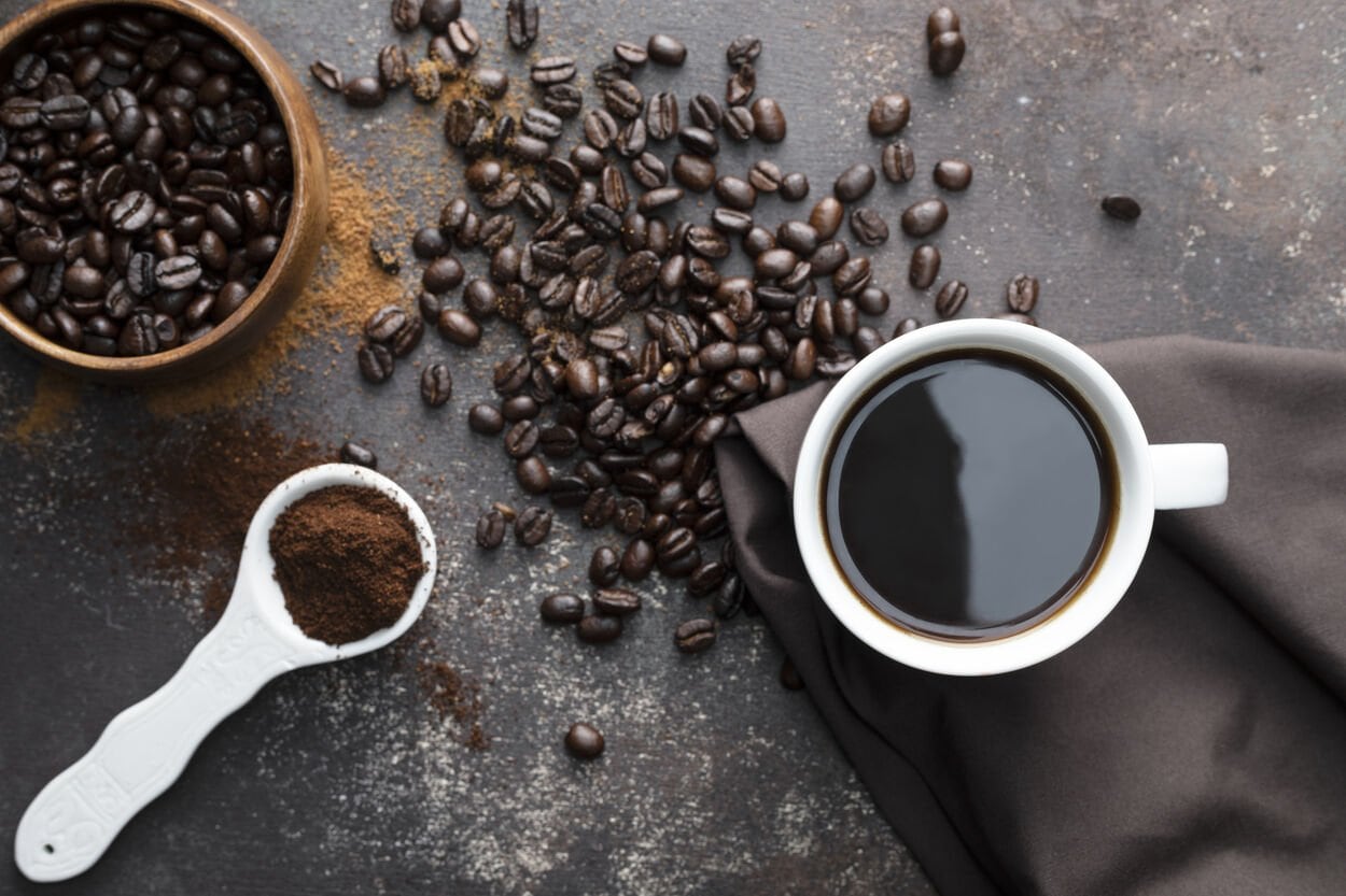 Een tafel vol koffie: koffiebonen, gemalen koffie en een kop koffie. Alles voor de huid!