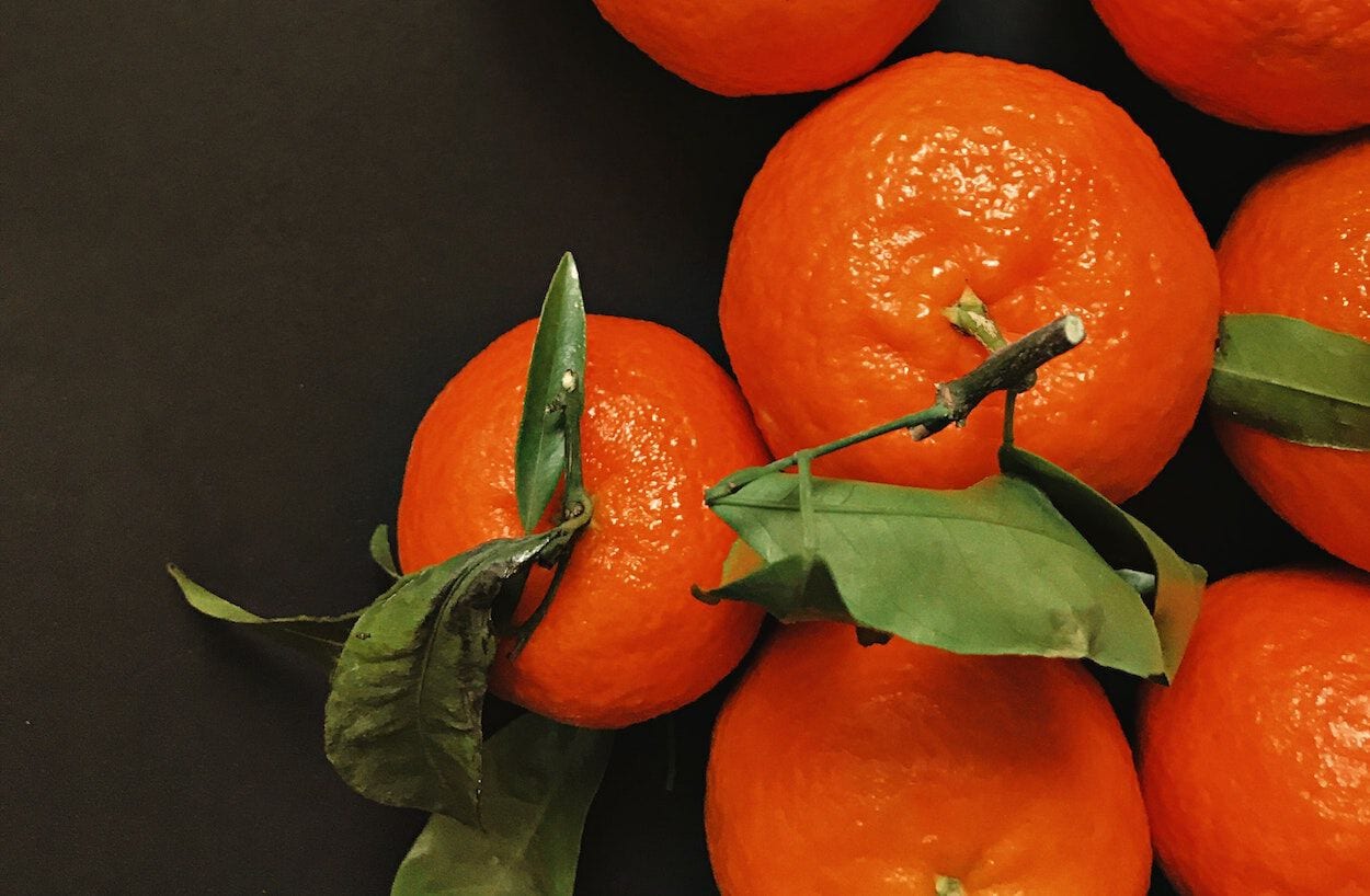 Een tros mandarijnen in de kleur oranje met groene blaadjes, dit fruitsoort is gezond en past is een gezond eetschema.