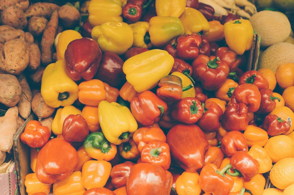 Heel veel rode, gele en oranje paprika's op een hoop bij elkaar