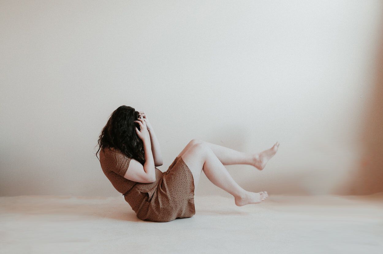 vrouw zit op grond met handen voor gezicht
