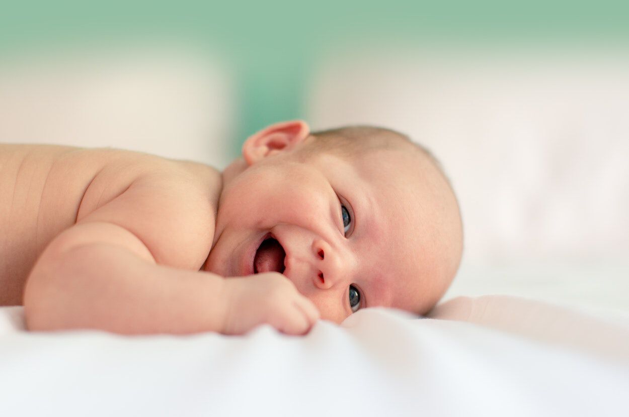 Lachende baby ligt op een zachte, witte ondergrond