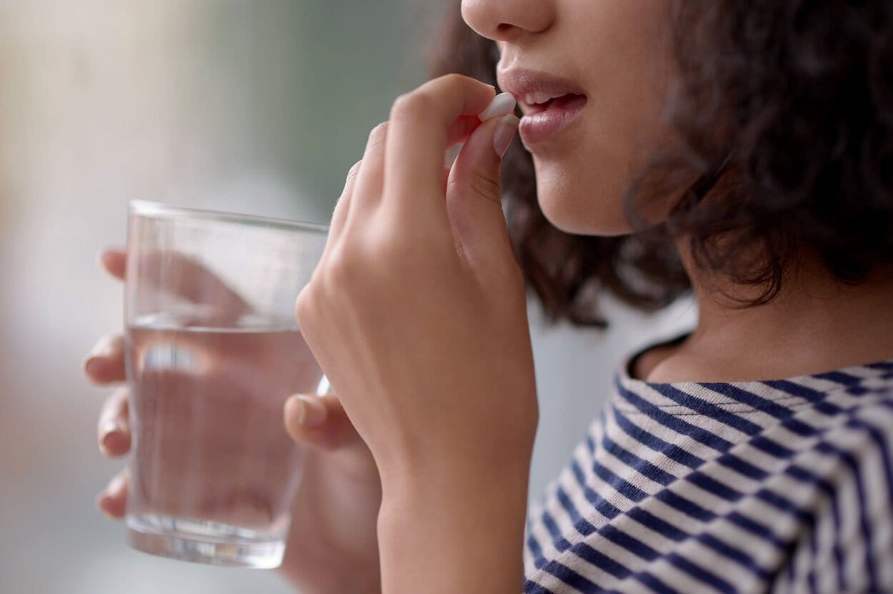 Vrouw die een vitamine B-Complex supplement inneemt met een glas water.