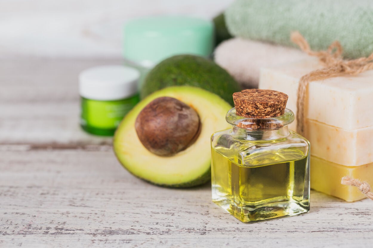 Een doorgesneden avocado naast een glazen potje met avocado-olie