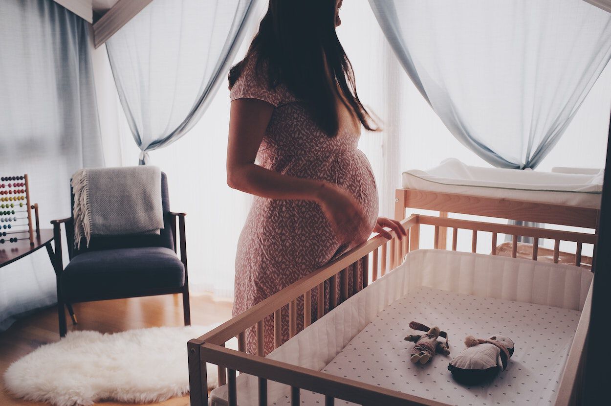 zwangere vrouw in roze jurk staat in kinderkamer