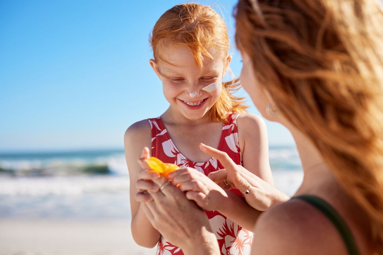 Moeder en kind op het strand. Moeder smeert haar kind in met zonnebrand.