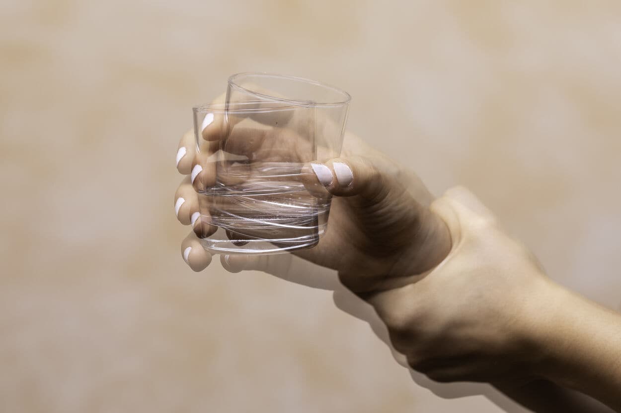 Iemand die met trillende handen een glas vasthoudt