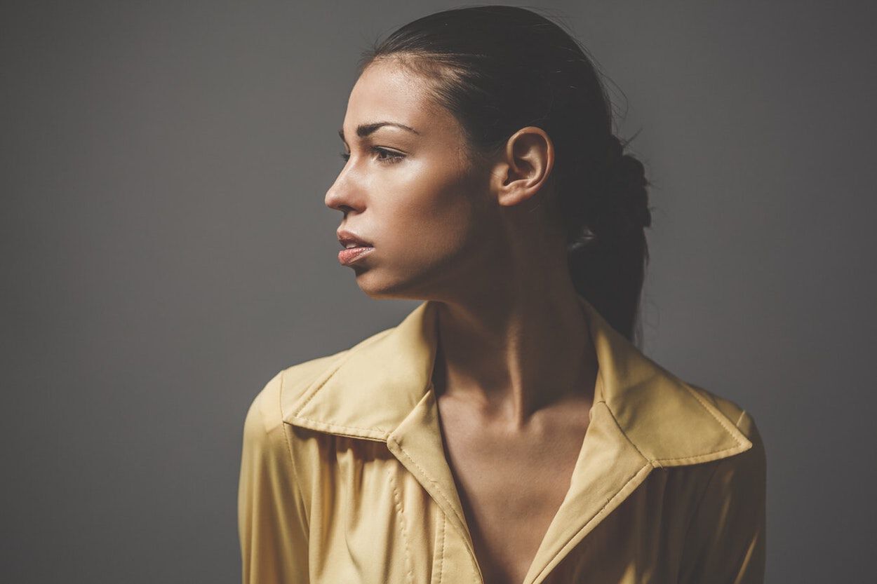 Vrouw met geel jasje kijkt naar de zijkant waarbij haar oor is te zien