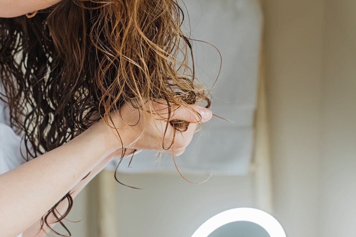 Vrouw die met haar handen conditioner in haar haar aanbrengt.