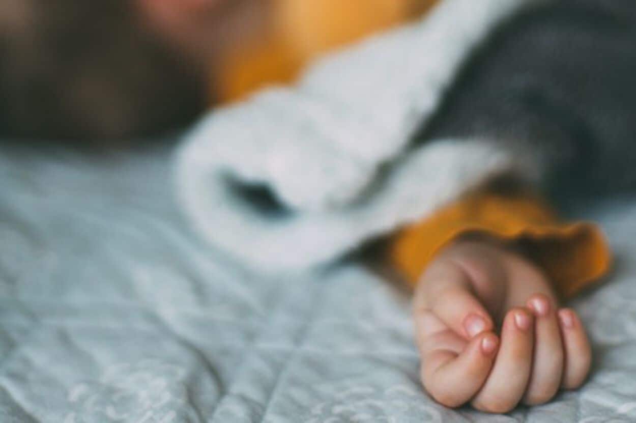 Handje van een peuter die in bed ligt. De peuter wil niet slapen.