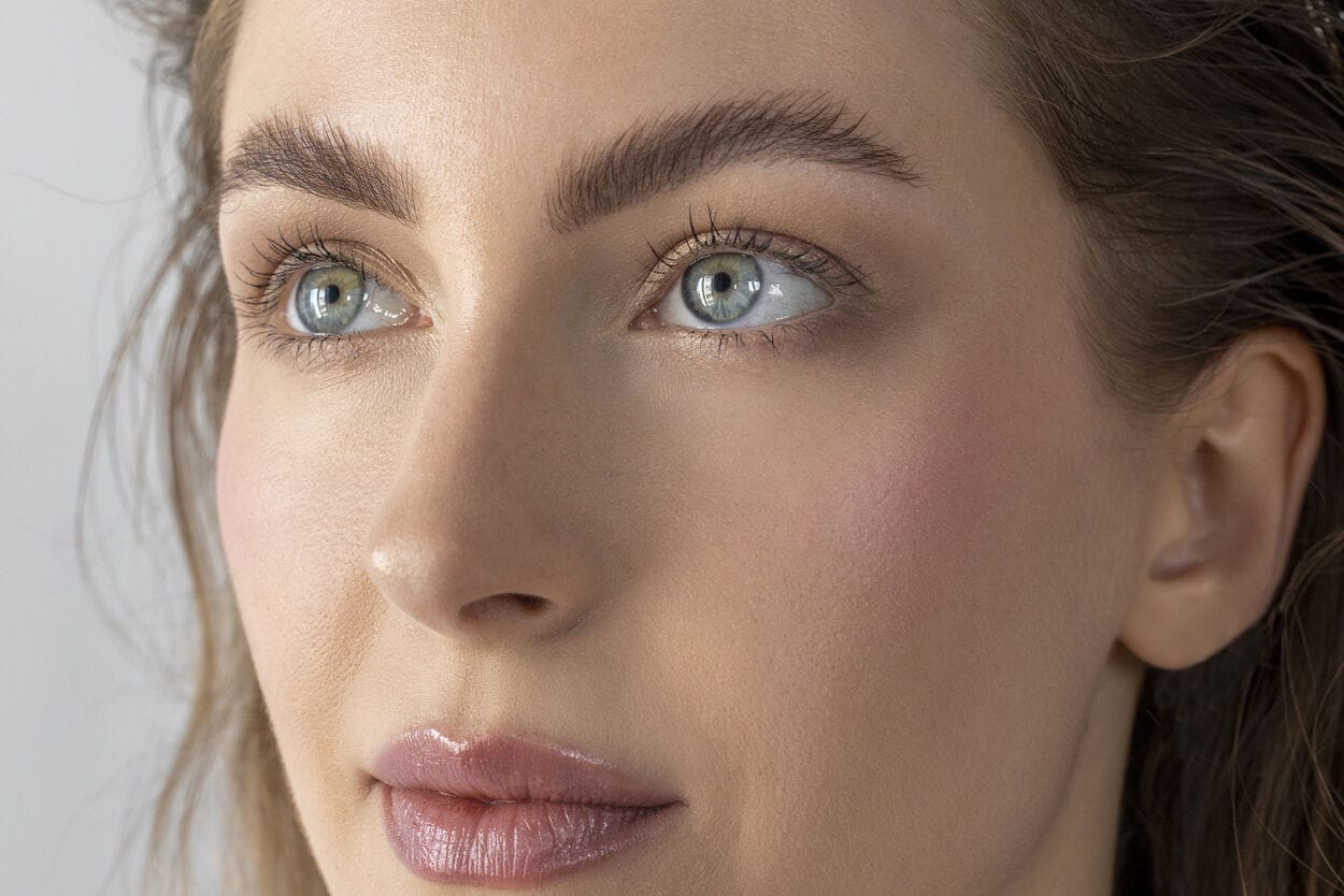 Vrouw die blush op de appeltjes van haar wangen heeft zitten, wat een warme, gezonde gloed geeft.