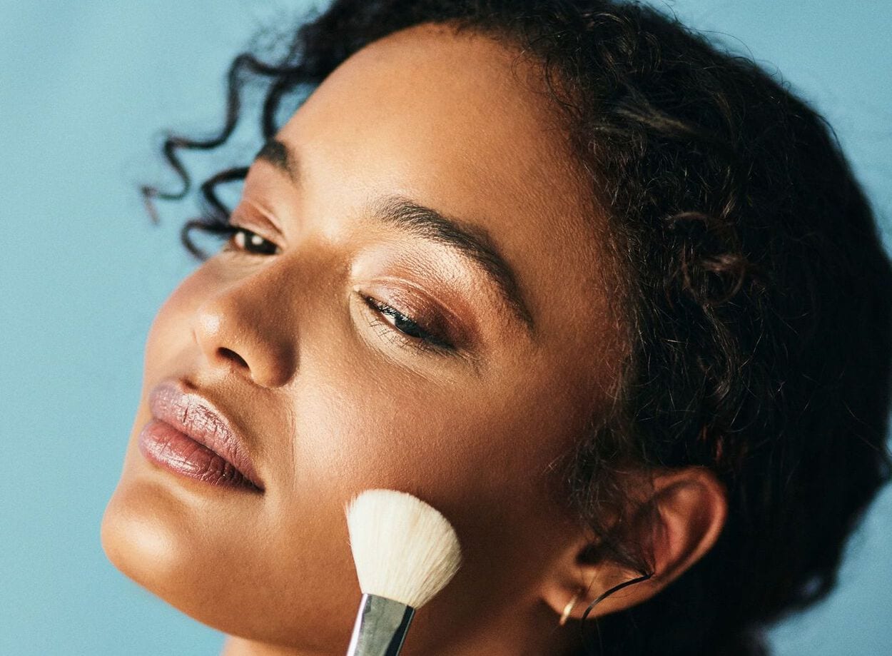 Vrouw die met een make-upborstel bronzer aanbrengt op haar wangen.