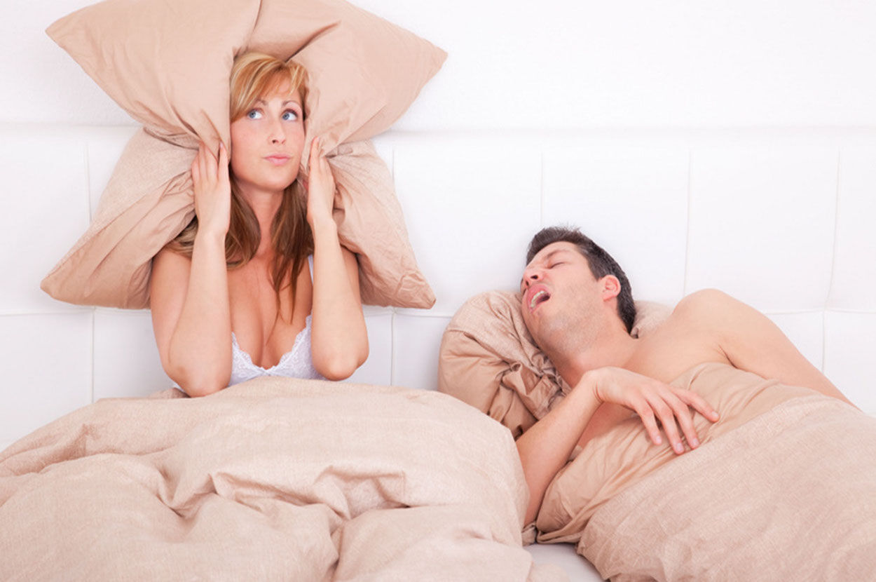 man snurkt in bed naast vrouw met kussen tegen haar oren