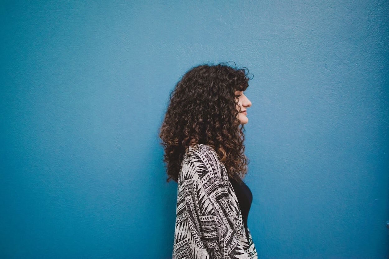 vrouw met krullen loopt langs blauwe muur