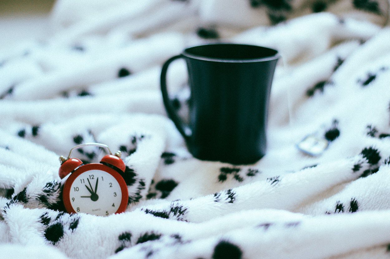 Een klein rood klokje op bed: de klok is een uur verzet door de wintertijd.