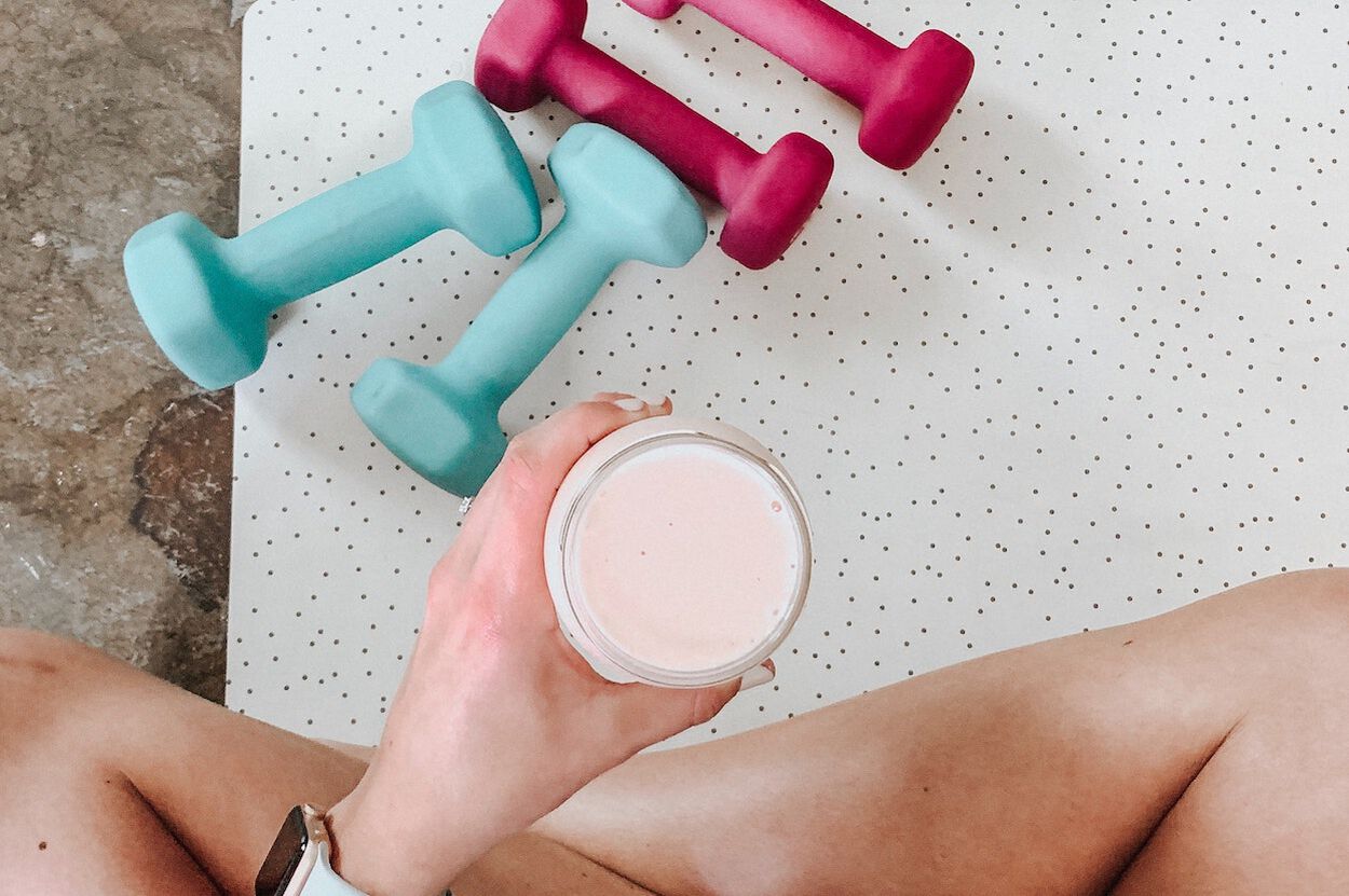 Vrouw die op haar yogamat een proteïneshake drinkt. Ze heeft ondergewicht en wil graag aankomen.