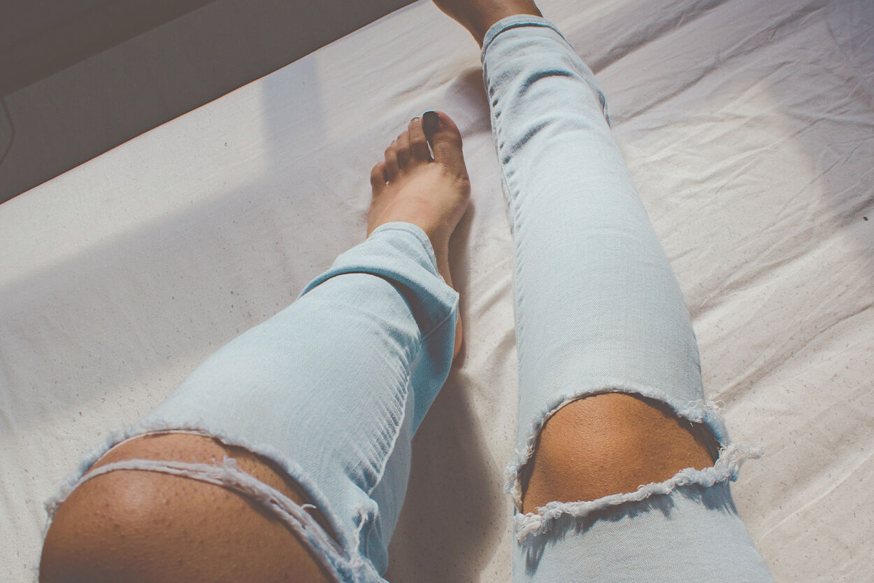 gescheurde broek met de benen van een vrouw met blote voeten