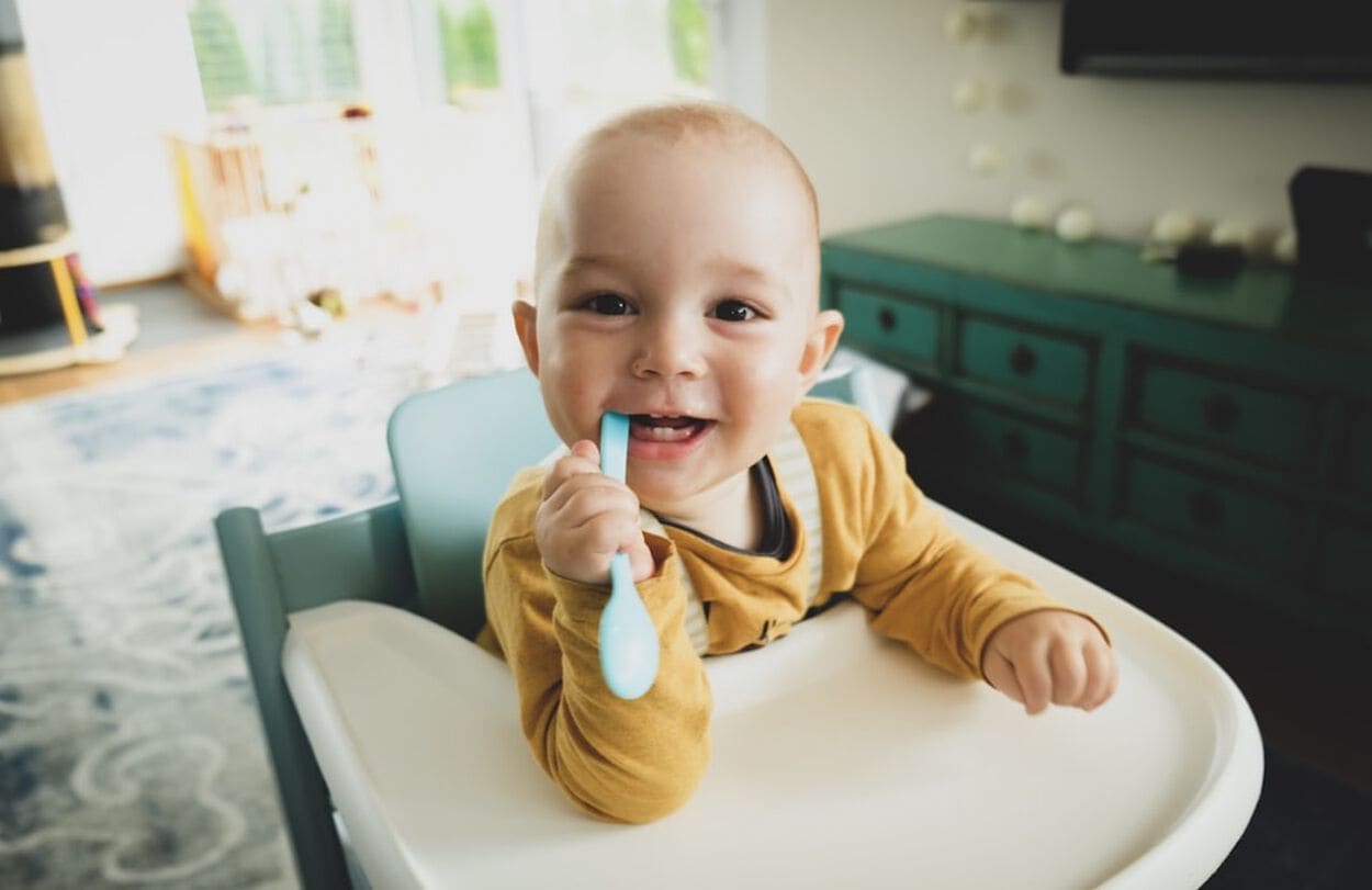 baby in kinderstoel met lepel in mond