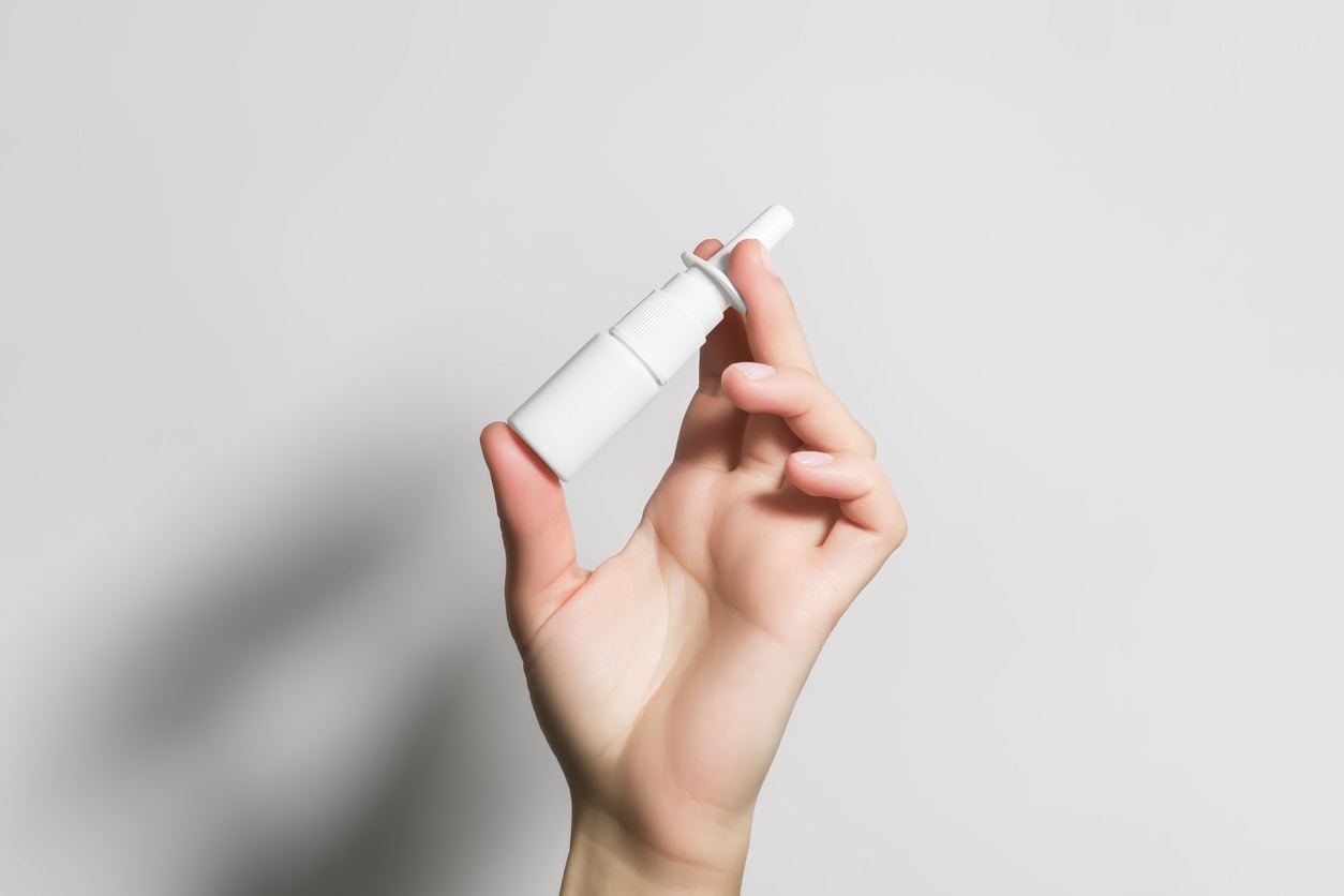 hand met neusspray op grijze achtergrond