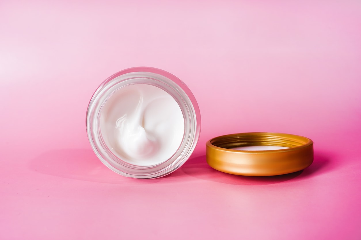 een potje dagcreme op z'n zij op roze achtergrond